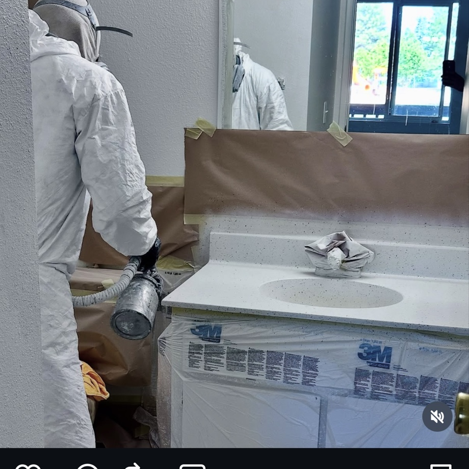 Technician spray-painting a bathroom vanity during a refinishing job